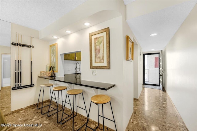 kitchen with a kitchen breakfast bar, a textured ceiling, sink, and kitchen peninsula