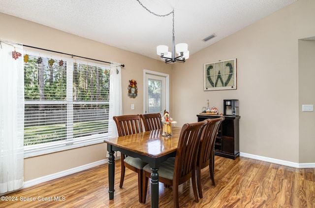 dining space featuring a textured ceiling, hardwood / wood-style floors, vaulted ceiling, and a notable chandelier