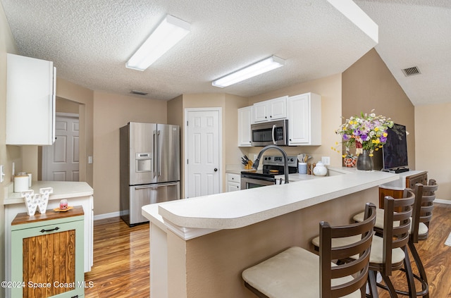 kitchen with a kitchen bar, kitchen peninsula, light hardwood / wood-style floors, and appliances with stainless steel finishes