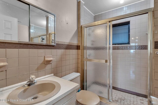 bathroom with tile walls, walk in shower, vanity, and toilet