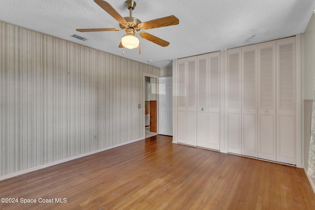 unfurnished bedroom with two closets, a textured ceiling, hardwood / wood-style flooring, and ceiling fan