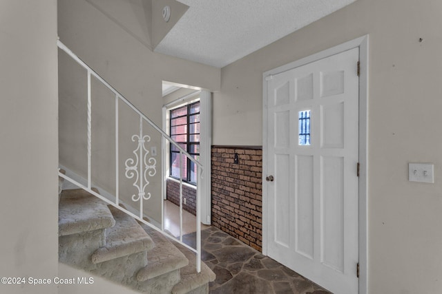 foyer featuring a textured ceiling and brick wall