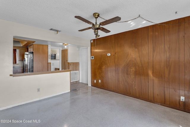 unfurnished living room with wood walls, ceiling fan, and a textured ceiling