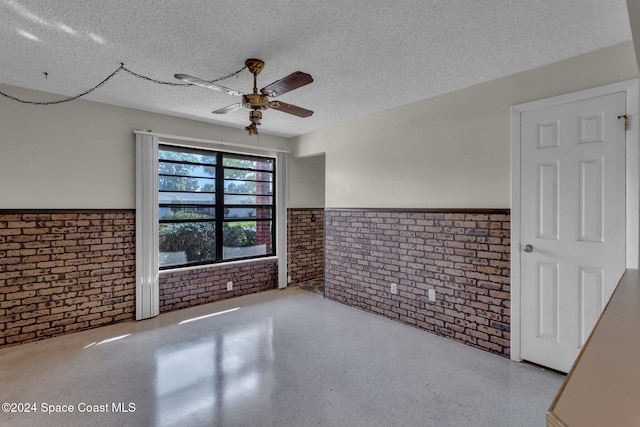 unfurnished room with ceiling fan, a textured ceiling, and brick wall