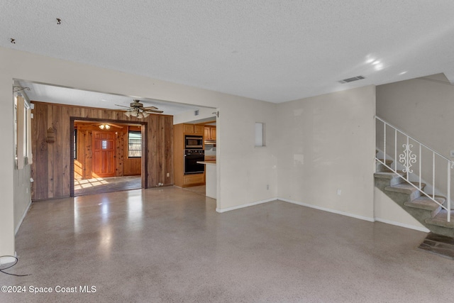 unfurnished living room with a textured ceiling, wooden walls, and ceiling fan