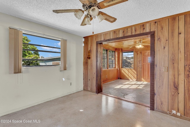 spare room with a textured ceiling, wooden walls, and ceiling fan