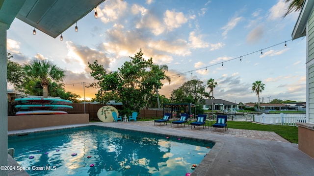 pool at dusk featuring a water view and a patio