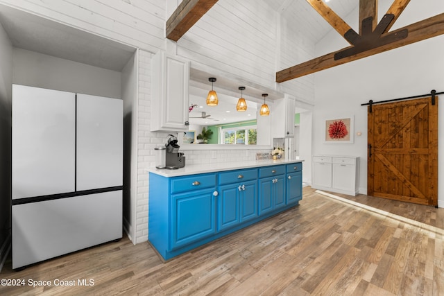 kitchen with a barn door, blue cabinetry, hanging light fixtures, and light hardwood / wood-style flooring