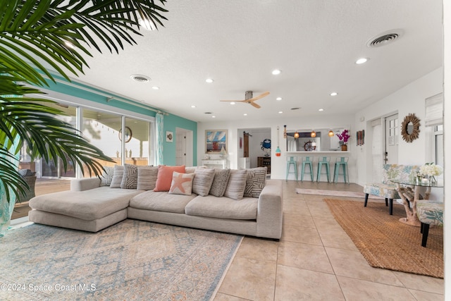 living room featuring ceiling fan, light tile patterned flooring, and a textured ceiling