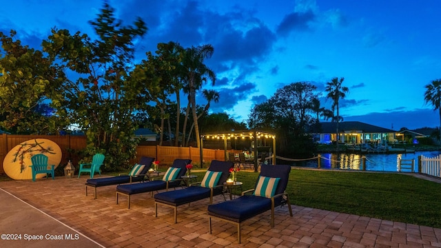 patio terrace at dusk featuring a lawn and a water view