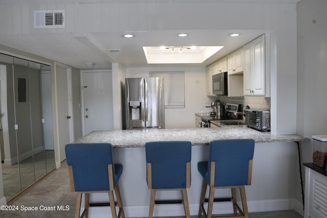 kitchen featuring white cabinets, a kitchen breakfast bar, kitchen peninsula, and appliances with stainless steel finishes