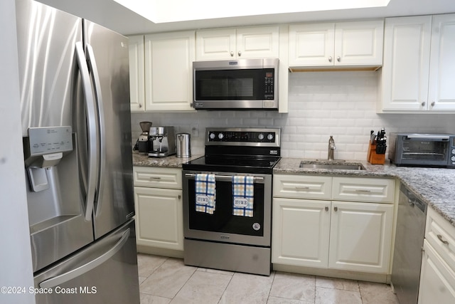 kitchen featuring stainless steel appliances, sink, backsplash, light stone countertops, and white cabinetry