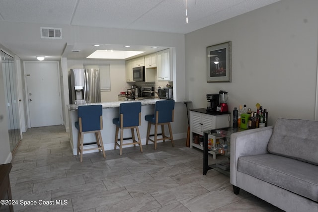 kitchen featuring stainless steel appliances, kitchen peninsula, backsplash, a breakfast bar, and white cabinetry