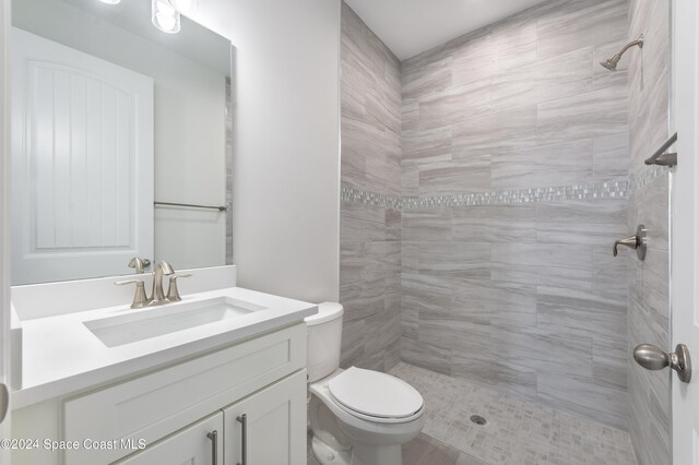 bathroom featuring a tile shower, vanity, and toilet