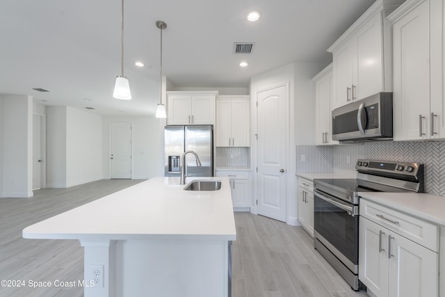 kitchen featuring white cabinets, light hardwood / wood-style flooring, a kitchen island with sink, pendant lighting, and appliances with stainless steel finishes