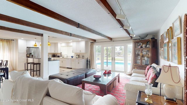 living room with beamed ceiling, track lighting, french doors, and a textured ceiling