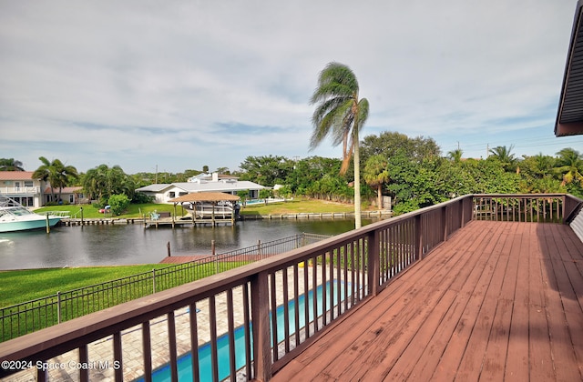 wooden terrace featuring a water view, a boat dock, and a fenced in pool