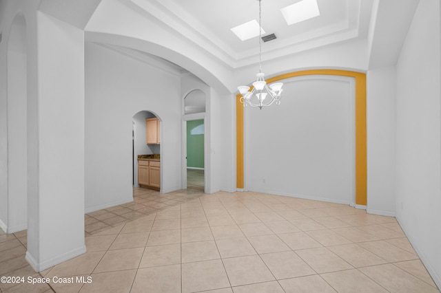 tiled spare room featuring an inviting chandelier and a tray ceiling