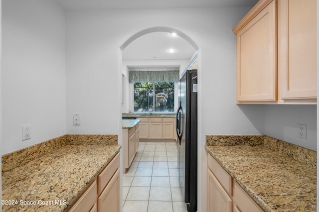 kitchen featuring light brown cabinets, light stone countertops, light tile patterned floors, and black refrigerator