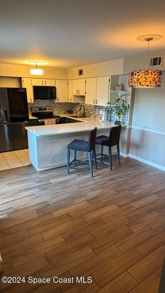 kitchen featuring kitchen peninsula, light wood-type flooring, white cabinets, and black appliances