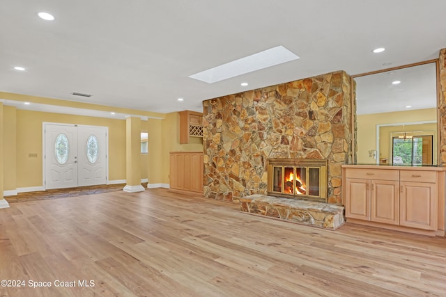 unfurnished living room with light wood-type flooring, a skylight, and a stone fireplace