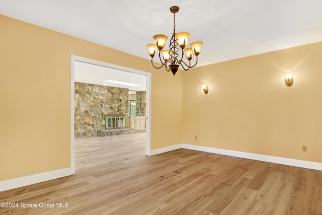 unfurnished dining area with a stone fireplace, a chandelier, and light hardwood / wood-style floors