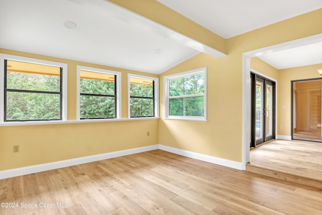 unfurnished room with vaulted ceiling with beams, light wood-type flooring, and a wealth of natural light