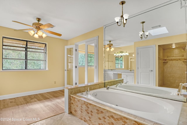 bathroom featuring ceiling fan with notable chandelier, hardwood / wood-style flooring, plenty of natural light, and a relaxing tiled tub