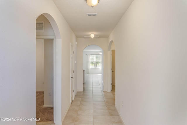 hall featuring light tile patterned flooring and a textured ceiling