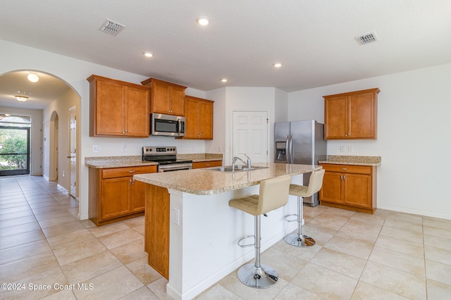 kitchen with a breakfast bar, a kitchen island with sink, sink, appliances with stainless steel finishes, and light tile patterned flooring