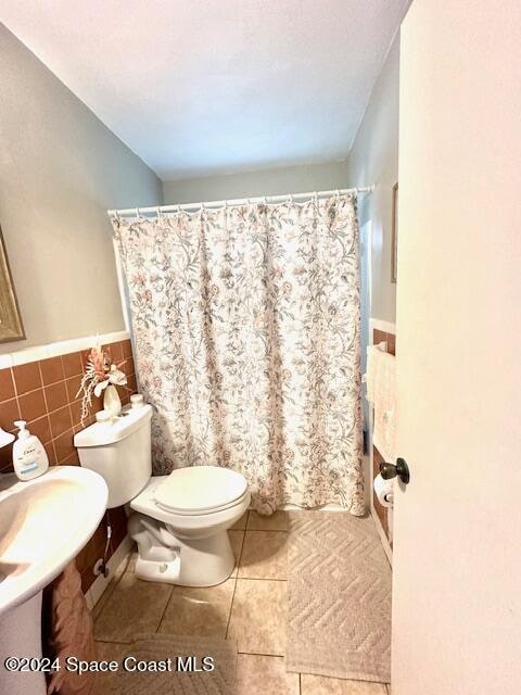 bathroom featuring tile patterned floors, curtained shower, toilet, and tile walls