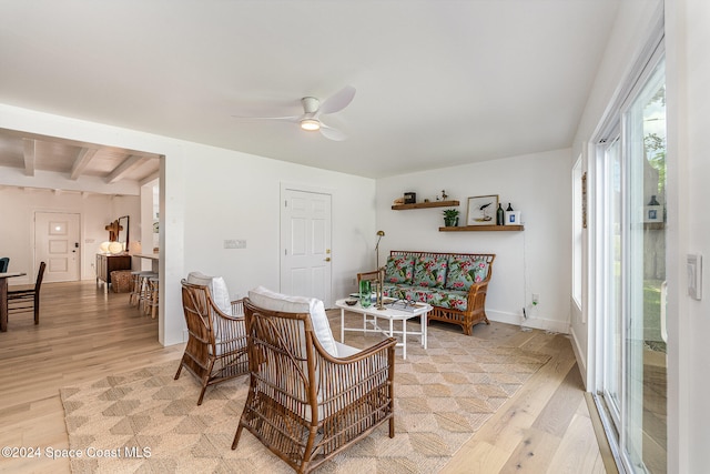 living room featuring beamed ceiling, light hardwood / wood-style floors, and ceiling fan