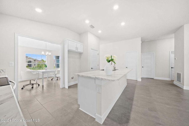 kitchen with a center island with sink, white cabinets, hanging light fixtures, a chandelier, and light stone countertops