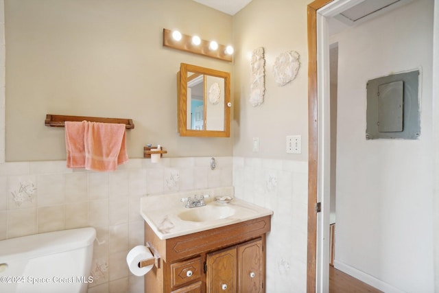 bathroom featuring vanity, electric panel, toilet, and tile walls