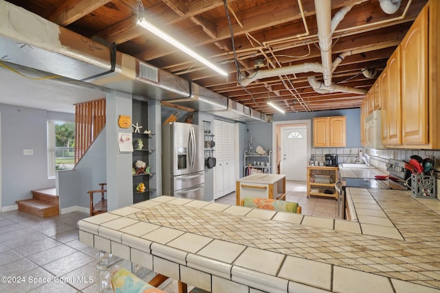 kitchen with tasteful backsplash, tile countertops, a kitchen island, and appliances with stainless steel finishes