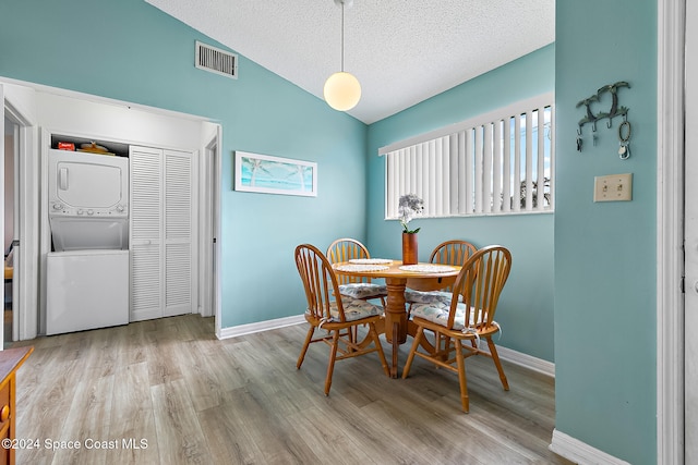 dining space with visible vents, stacked washer / drying machine, vaulted ceiling, a textured ceiling, and light wood-type flooring