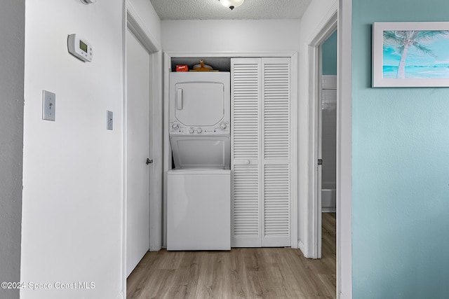 clothes washing area featuring a textured ceiling, laundry area, light wood finished floors, and stacked washer / drying machine