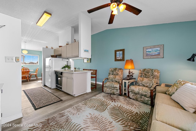 living area featuring light wood finished floors, lofted ceiling, ceiling fan, a textured ceiling, and baseboards