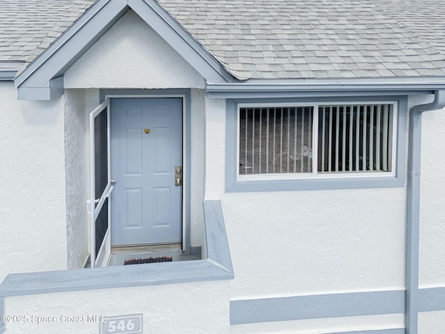 property entrance featuring a shingled roof and stucco siding