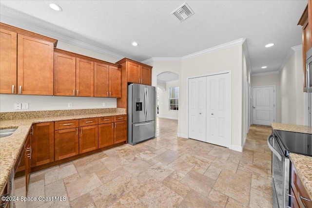 kitchen with light stone counters, ornamental molding, a textured ceiling, and appliances with stainless steel finishes