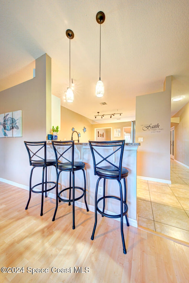 kitchen featuring track lighting, kitchen peninsula, a kitchen bar, light wood-type flooring, and pendant lighting