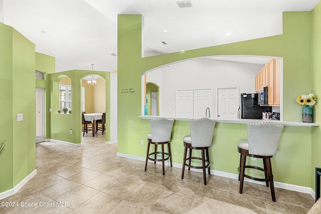 kitchen with lofted ceiling, black fridge, light tile patterned floors, light brown cabinetry, and a kitchen bar