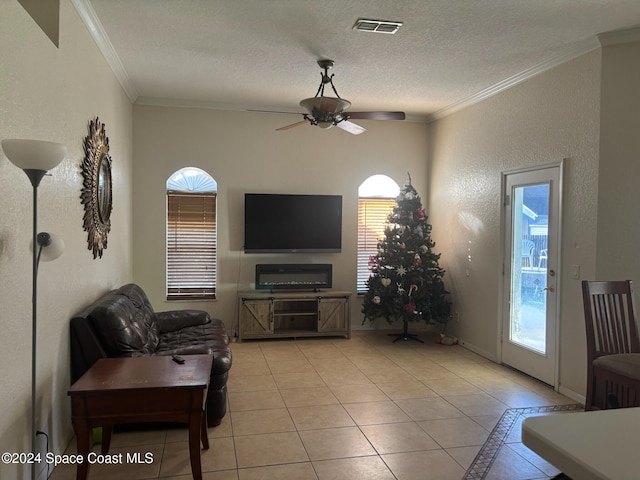 tiled living room featuring ceiling fan, ornamental molding, and a textured ceiling