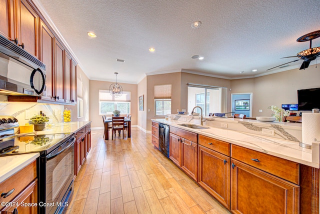 kitchen featuring decorative light fixtures, sink, light stone counters, black appliances, and light wood-type flooring