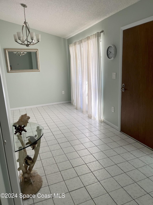 empty room featuring light tile patterned floors, a textured ceiling, and a notable chandelier