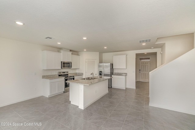 kitchen with a center island with sink, sink, light stone countertops, white cabinetry, and stainless steel appliances