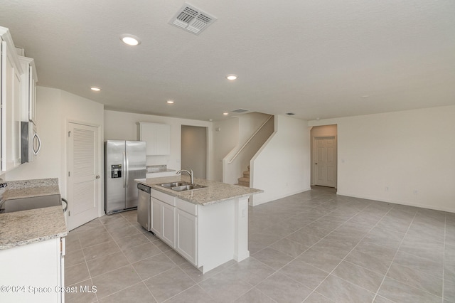 kitchen featuring appliances with stainless steel finishes, light stone counters, a kitchen island with sink, sink, and white cabinetry