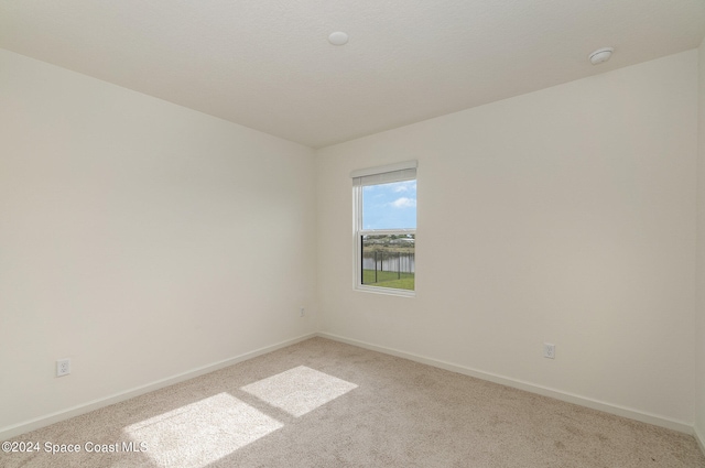 empty room featuring a water view and light colored carpet