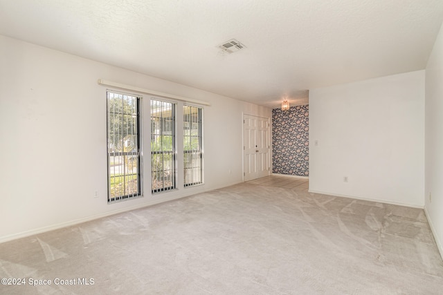 spare room with light carpet, a textured ceiling, and a notable chandelier