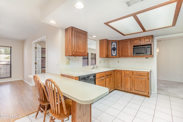 kitchen with a kitchen bar, sink, black appliances, kitchen peninsula, and light wood-type flooring